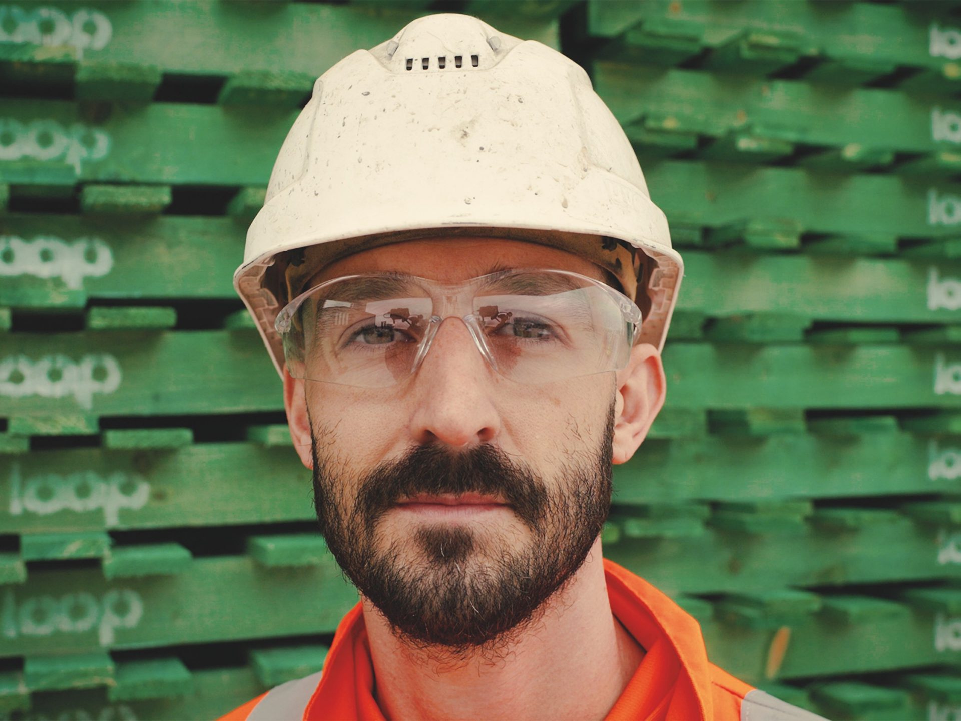 Man in hard hat and protective glasses standing in front of green pallets