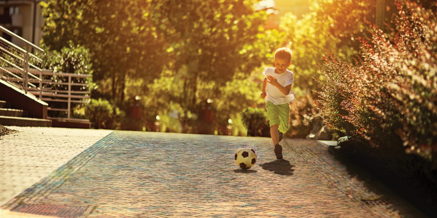 Child playing with football on clay paved area
