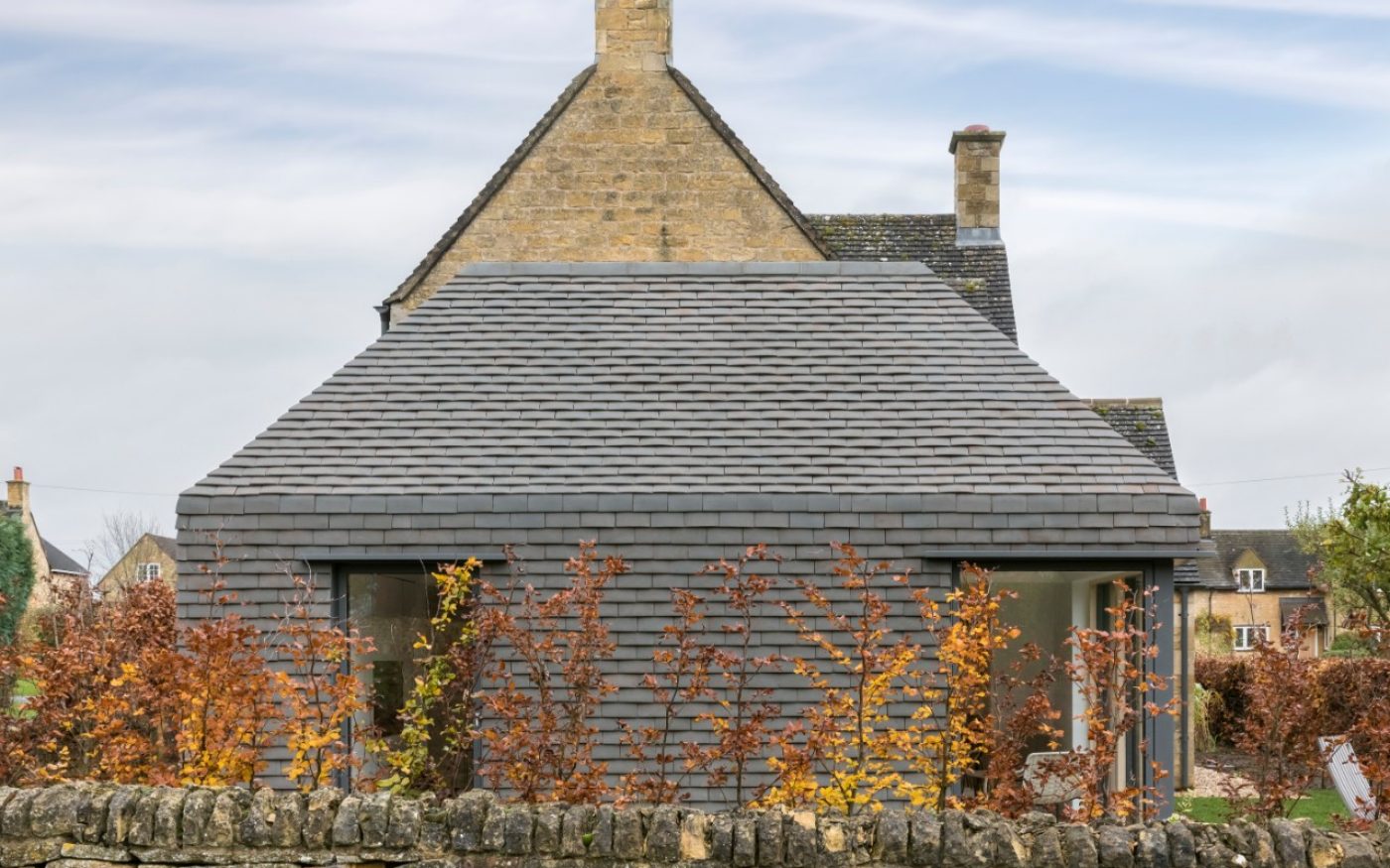 Hedge in front of modern vertical tiled extension on traditional house